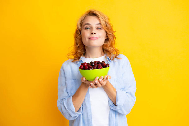 Attractive young woman eating fresh cherry. Healthy summer fruits. Yellow background. Beautiful woman posing with a cherry, girl with cherry promoting. - Foto, afbeelding