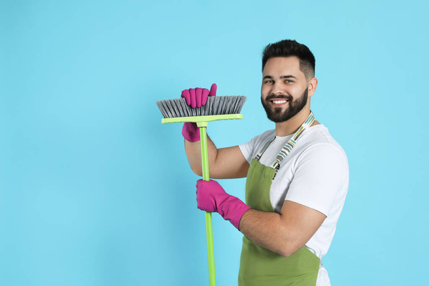 Young man with green broom on light blue background, space for text - Fotografie, Obrázek