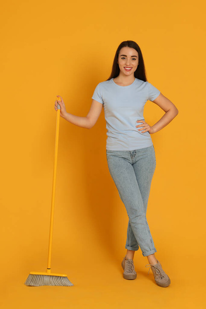 Beautiful young woman with broom on yellow background - Foto, Imagen