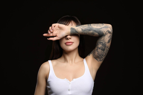 Beautiful woman with tattoos on arm against black background - Foto, Imagen
