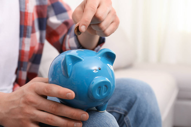Man putting coin in piggy bank at home, closeup - Foto, Imagen