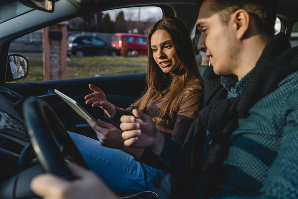 Man and woman young couple or friends male and female boyfriend and girlfriend using digital tablet for navigation searching map for direction arguing while travel in car real people copy space - Zdjęcie, obraz