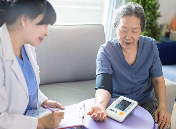 Médico cuidador asiático examinar paciente mayor uso manómetro de presión arterial. - Foto, Imagen