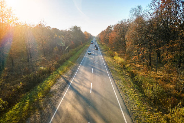Vista aérea da estrada interurbana com carros de condução rápida entre árvores florestais de outono ao pôr do sol. Vista superior do drone do tráfego rodoviário à noite - Foto, Imagem