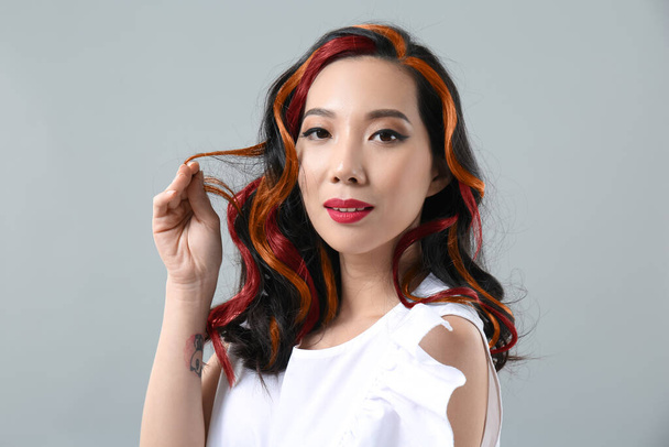 Joven mujer asiática con hermoso pelo colorido sobre fondo gris - Foto, imagen