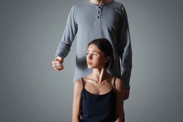 Scared woman and her abuser on grey background. Violence concept - Photo, Image