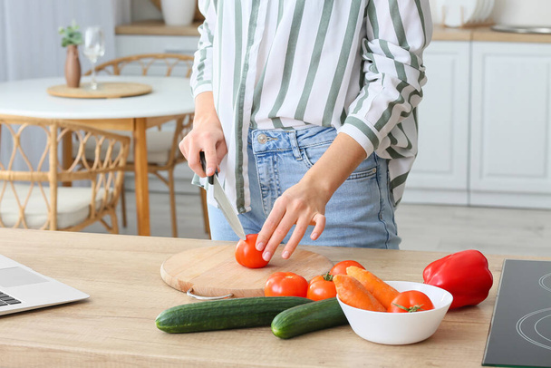 Молодая женщина режет свежий помидор на кухне, крупным планом - Фото, изображение