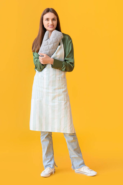 Pretty young woman with oven mitten on yellow background - Photo, Image