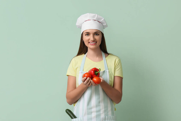 Female chef with red bell pepper and tomatoes on green background - Photo, Image