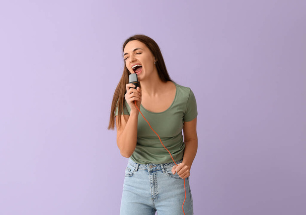Hübsche junge Frau mit Mikrofon singt auf fliederfarbenem Hintergrund - Foto, Bild