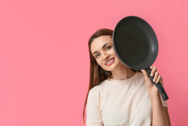 Красивая молодая женщина с сковородкой на розовом фоне - Фото, изображение