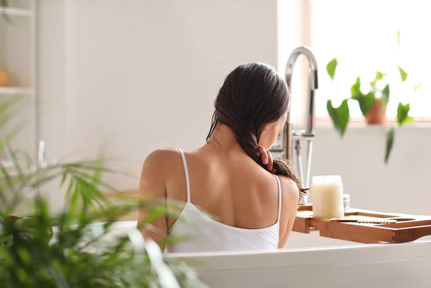 Jeune femme appliquant de l'huile de coco sur ses cheveux dans la salle de bain - Photo, image