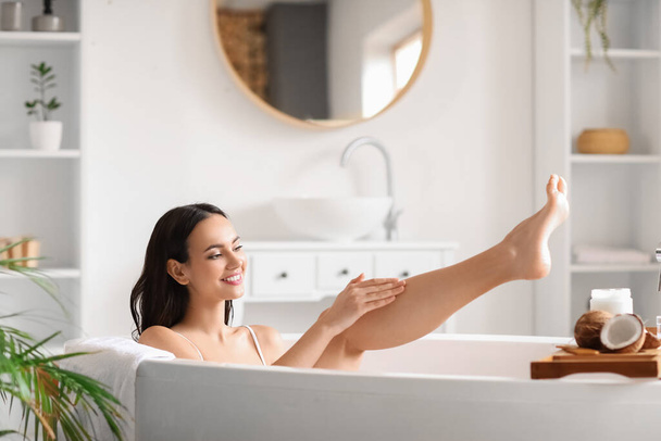 Hermosa mujer aplicando aceite de coco en su pierna en el baño - Foto, Imagen