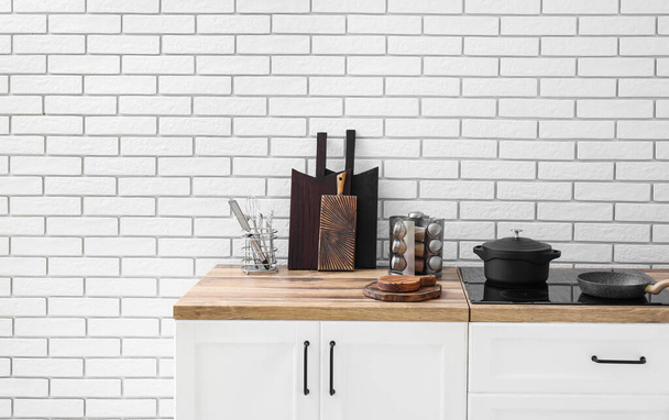 Доски для резки и кухонная утварь на прилавке возле стены из белого кирпича - Фото, изображение