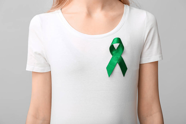 Γυναίκα σε λευκό t-shirt με πράσινη κορδέλα σε γκρι φόντο. Έννοια του καρκίνου του ήπατος - Φωτογραφία, εικόνα