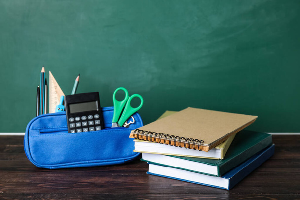 Pencil case with school stationery and books on table near green chalkboard - Foto, Imagen