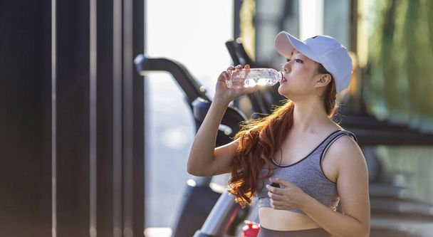 Asiatico donna godere di mattina esercizio in palestra, mentre avere una pausa per bere acqua minerale per rinfresco e reidratazione concetto - Foto, immagini