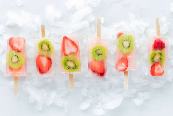 Une rangée de glaces rafraîchissantes aux kiwis aux fraises sur un lit de glace. - Photo, image
