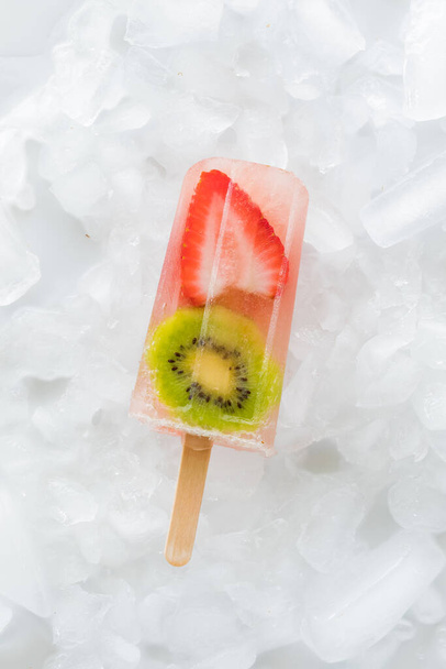 A single strawberry kiwi popsicles isolated on a bed of ice. - Foto, Bild