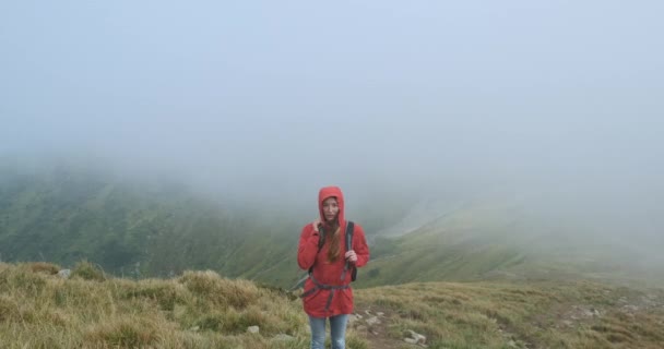 Woman look into the camera, standing on the edge of the mountain in a gray cloud. Movement of fog on the background. Stormy weather at the summit. Medium shot, spring summer, Carpathians, Ukraine. - Video