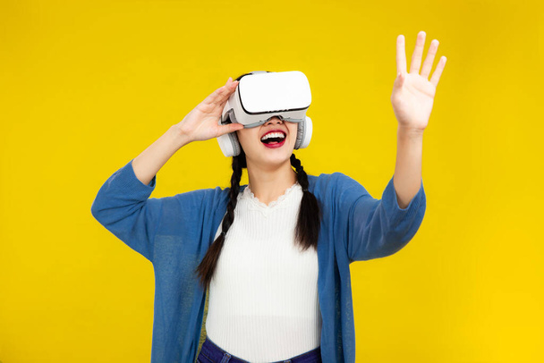 Metaverse Concepts, Asian woman in vr glasses isolated yellow background, playing video games with virtual reality headset, People emotions concept. - Photo, Image