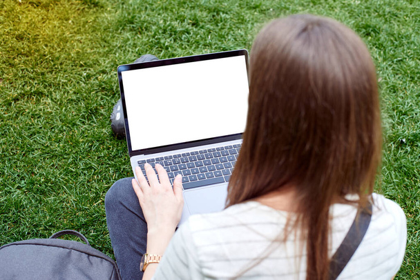  女性は公園の新鮮な空気中のノートパソコンで作業し、芝生の上に座って - 写真・画像