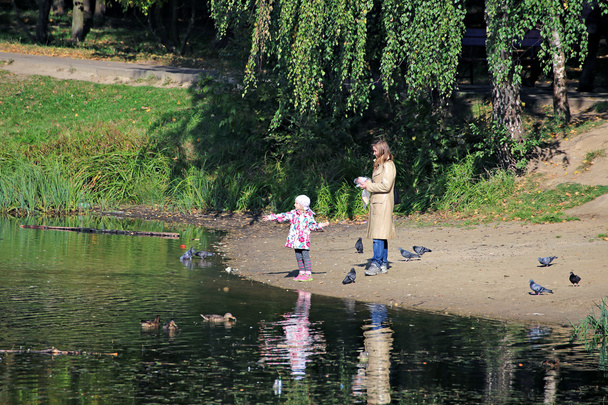 Дівчина з матір'ю годувати птахів на ставку - Фото, зображення