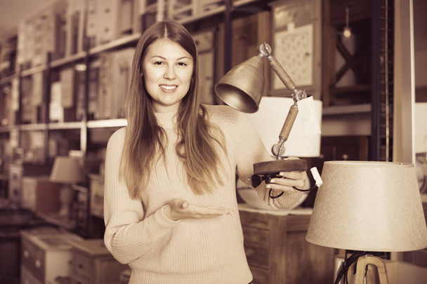 Portrait of cheerful woman buyer choosing modern lamp in furniture shop - Foto, Bild