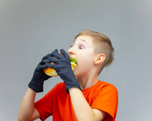 el muchacho abultó sus ojos y muerde una hamburguesa jugosa enorme con una ensalada dentro - Foto, Imagen
