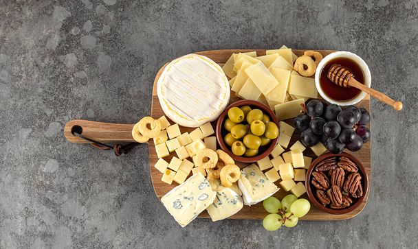 Tasty cheese board with berries, honey, nuts, olives, and cheese varieties - Photo, Image