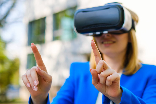Business woman using VR goggles touching the simulation screen in the park - Photo, Image