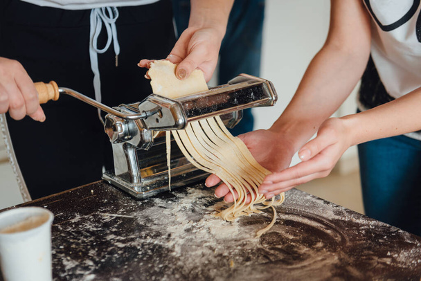 Homemade italian pasta preparation with paste machine. Close-up of two girls hands cooking traditional italian pasta - Fotó, kép