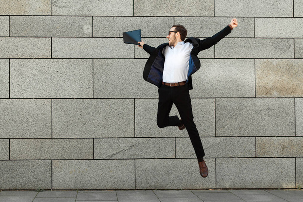 Young businessman in a suit jumping for joy, success, victory. - Foto, imagen