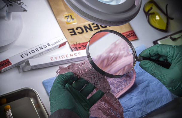 Policjant bada bieliznę ofiary gwałtu szkłem powiększającym, by zbadać DNA w laboratorium kryminalistycznym. - Zdjęcie, obraz