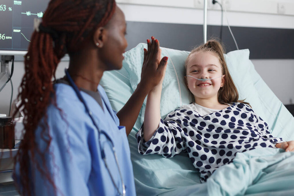 Infermiera ospedaliera highfive bambino malato mentre in sala trattamento paziente. - Foto, immagini