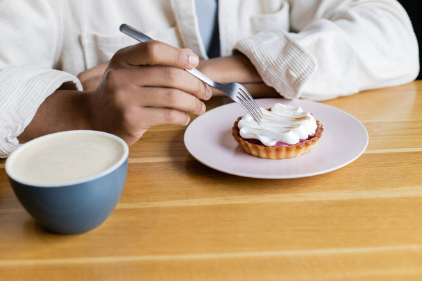 обрізаний вид на афроамериканця, що тримає виделку біля пирога і чашку капучино
  - Фото, зображення