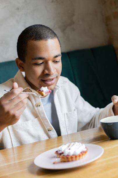 jong Afrikaans amerikaanse man eten smakelijke taart in coffeeshop - Foto, afbeelding