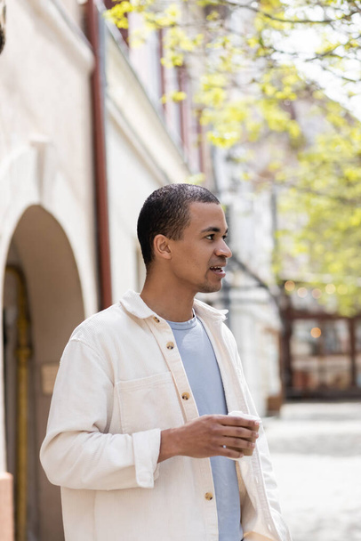 african american man in shirt jacket holding takeaway beverage in urban city  - Foto, Bild