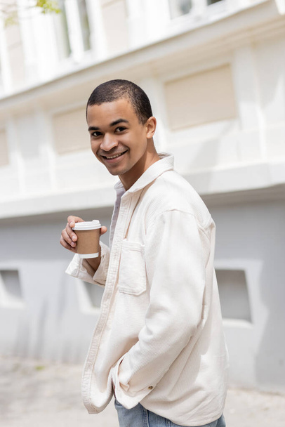 radosny Afrykański Amerykanin w koszuli, trzymający kawę na wynos i spacerujący po mieście.  - Zdjęcie, obraz