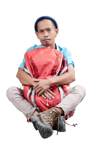 Asian man with a beanie hat hugging his a backpack sitting isolated over white background - 写真・画像