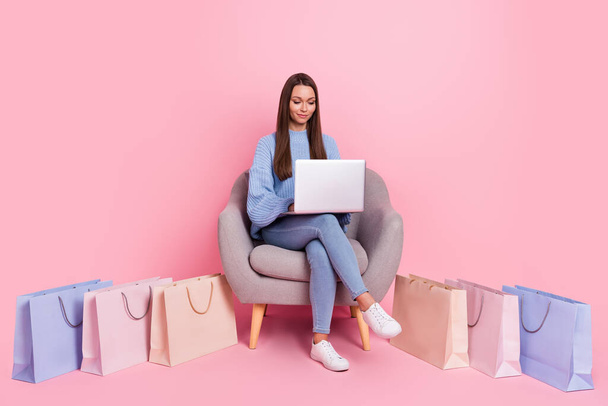 Фотографія повного тіла молодої жінки, сидячи в магазині крісел, використовують ноутбук ізольований на фоні рожевого кольору
 - Фото, зображення