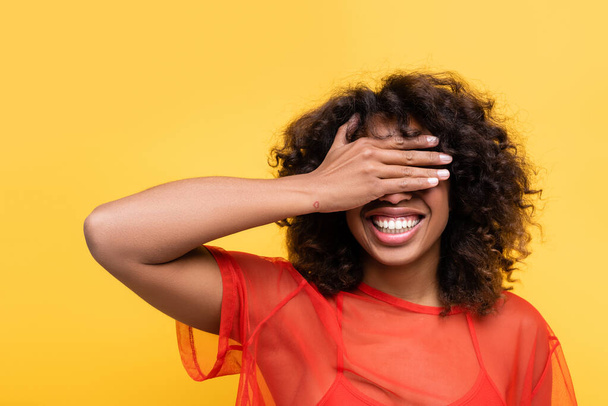 cheerful african american woman covering eyes with hand isolated on yellow - Foto, Imagem