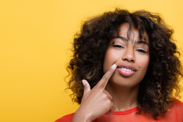cheerful african american woman pointing with finger at own smile isolated on yellow - Foto, afbeelding