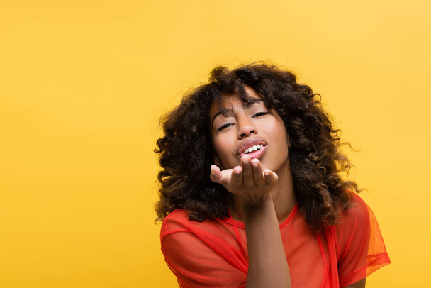 pretty and smiling african american woman blowing air kiss isolated on yellow - Fotografie, Obrázek