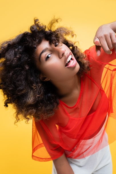 excited african american woman looking at camera and pointing with finger isolated on yellow - 写真・画像