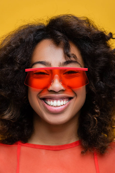 portrait of smiling brunette african american woman in stylish sunglasses isolated on yellow - Photo, Image