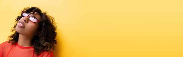 Африканська американка з кучерявим волоссям в модних сонцезахисних окулярах на жовтому прапорі - Фото, зображення