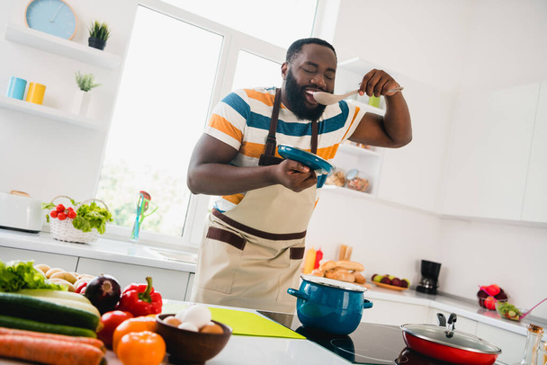 Photo of young cheerful guy good mood cooking dinner taste yummy fresh soup cuisine culinary indoors - Fotó, kép