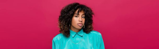 brunette african american woman in cyan blouse looking at camera isolated on pink, banner - Foto, afbeelding