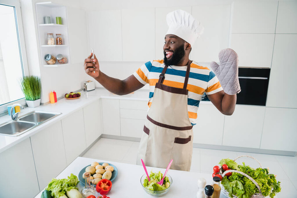 Portrait of excited positive handsome guy prepare salad arm waving make selfie photo free time house inside - Фото, изображение
